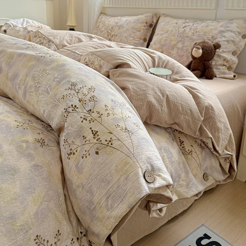 Beige floral patterned comforter on a bed with a teddy bear and small round object.

