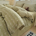 Green floral bedspread on a bed with a teddy bear and mug, in a softly lit room.

