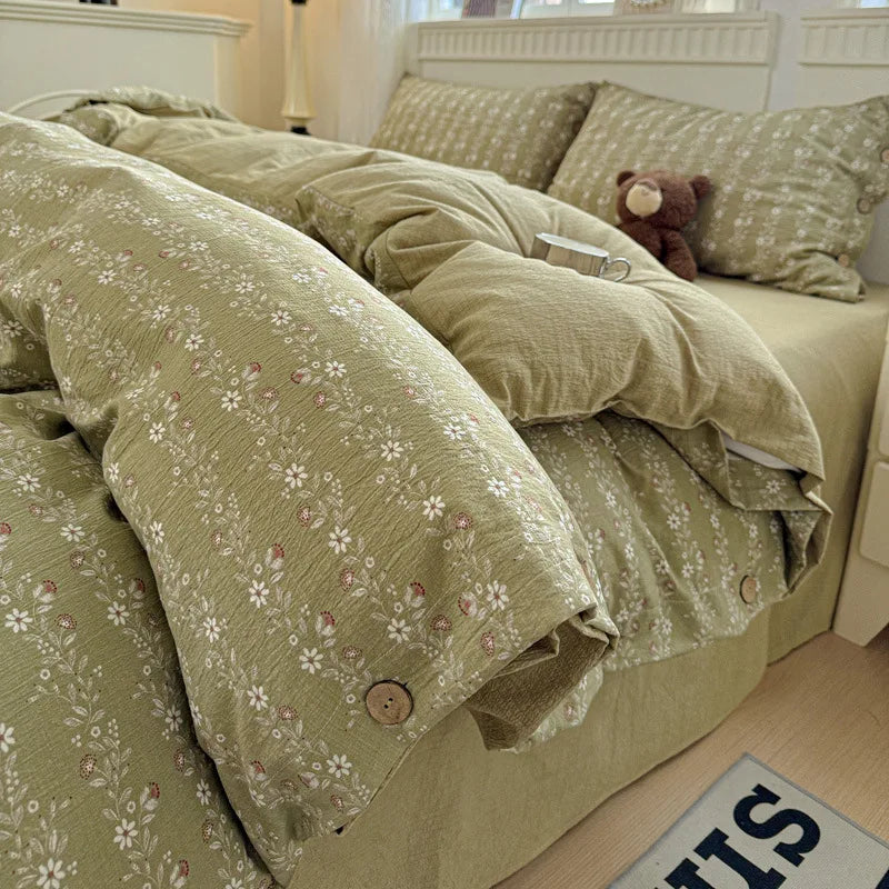 Green floral bedspread on a bed with a teddy bear and mug, in a softly lit room.

