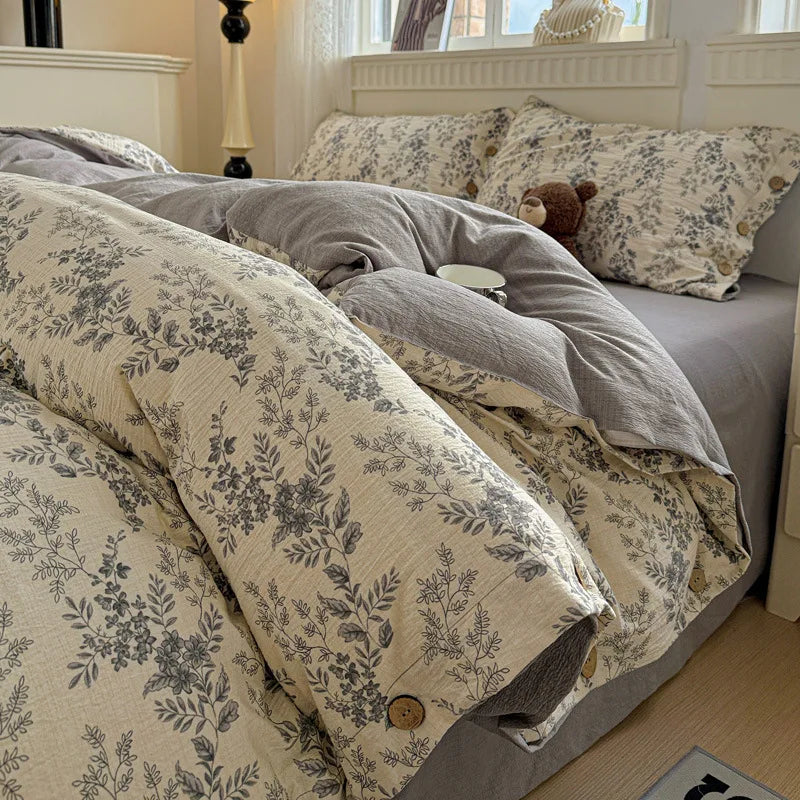 Floral and gray bedding on a bed with a teddy bear and small cup.

