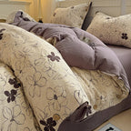 A cozy bed dressed in a beige and dusty purple floral bedding set, with matching pillows and a duvet featuring dark purple floral outlines and small wooden buttons.

