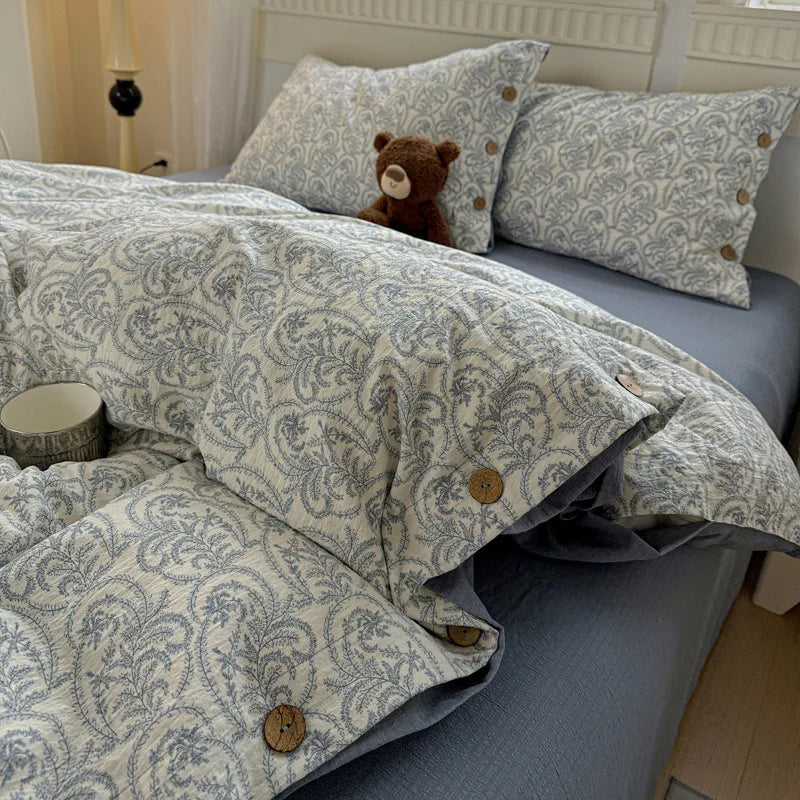 Bed with patterned duvet and pillows, featuring a teddy bear.

