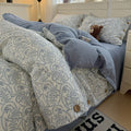 Bed with paisley patterned comforter and blue coverlet, teddy bear, and decorative pillows.

