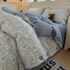 Bed with paisley patterned comforter and blue coverlet, teddy bear, and decorative pillows.

