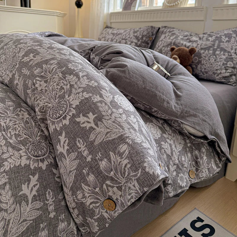 Gray floral-patterned comforter on a bed with pillows and a teddy bear.

