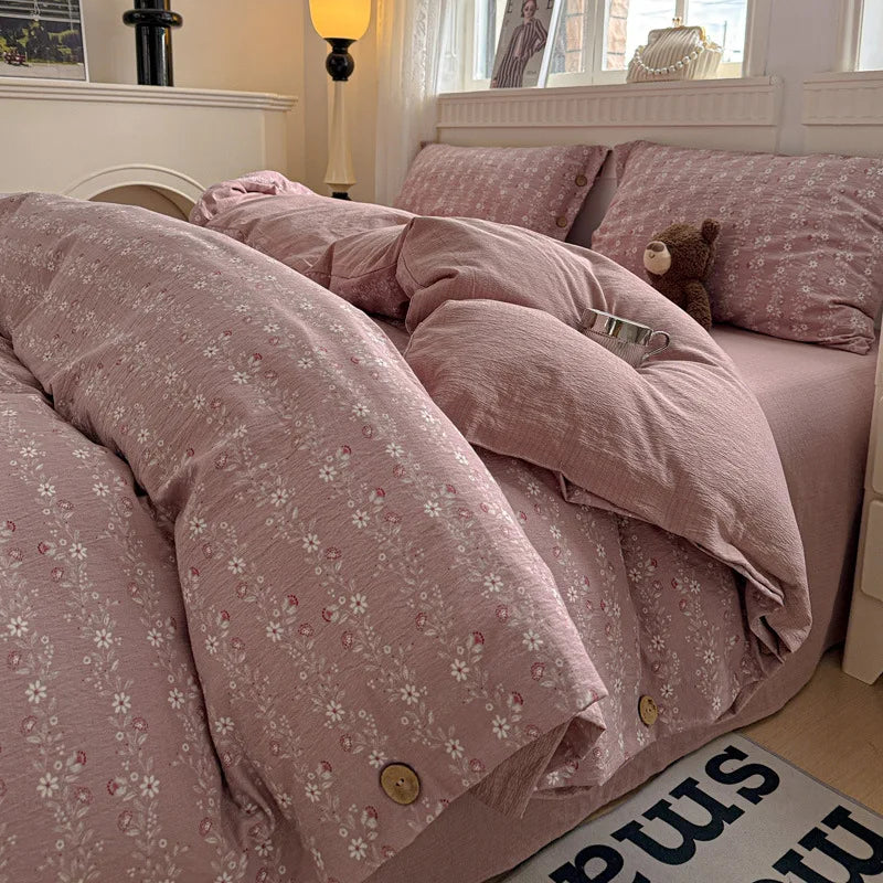 Pink floral bedspread on a bed with a teddy bear, in a softly lit bedroom.

