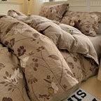 Floral patterned comforter on a bed with pillows and a teddy bear.

