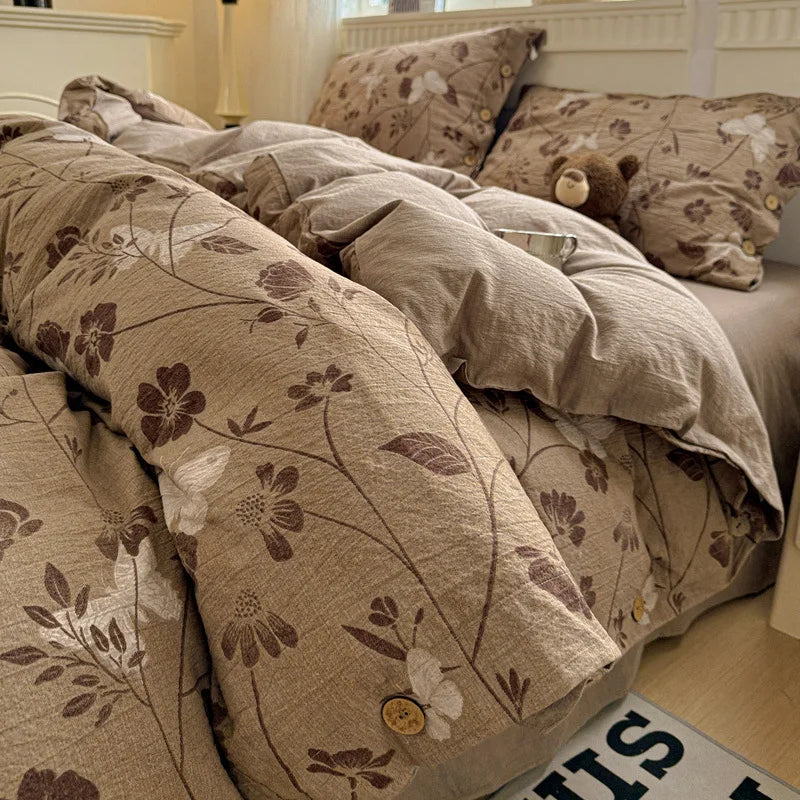 Floral patterned comforter on a bed with pillows and a teddy bear.

