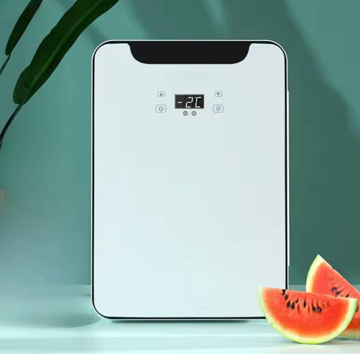 A white rectangular countertop appliance with rounded corners, a black top panel, and a small digital temperature display reading 26°C. The appliance is photographed on a light surface against a soft teal background, with green leaves at the upper left and watermelon slices at the lower right.

