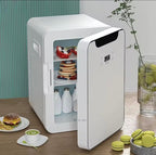A compact white mini refrigerator with its door open, shown on a tabletop with food items inside and around it, including pancakes with fruit, milk bottles, a burger, macarons, and a glass of iced tea.

