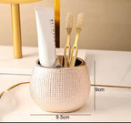 A textured metallic gold toothbrush holder cup on a white surface, containing a white toothpaste tube and two gold toothbrushes. Black measurement lines and text indicate dimensions of 9cm height and 9.

