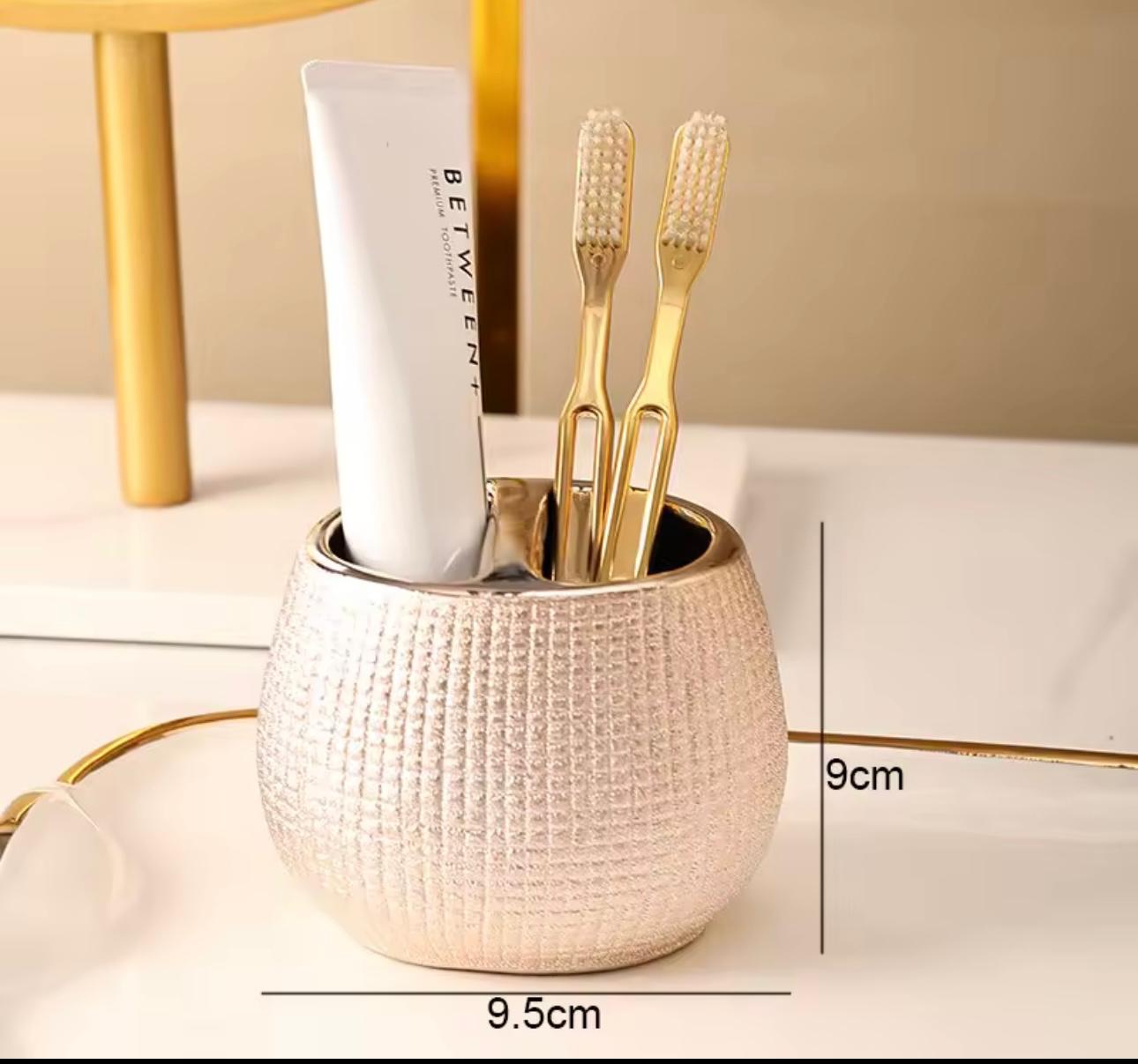 A textured metallic gold toothbrush holder cup on a white surface, containing a white toothpaste tube and two gold toothbrushes. Black measurement lines and text indicate dimensions of 9cm height and 9.


