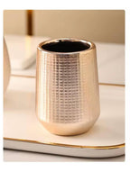 A textured metallic gold cup with a hammered pattern, sitting on a white tray with gold trim.

