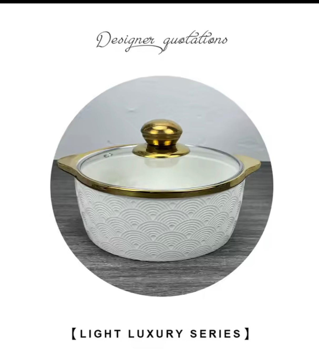 A white ceramic lidded casserole dish with a gold-trimmed glass lid and gold knob, shown inside a circular frame on a gray wood-textured background with decorative text above and below.

