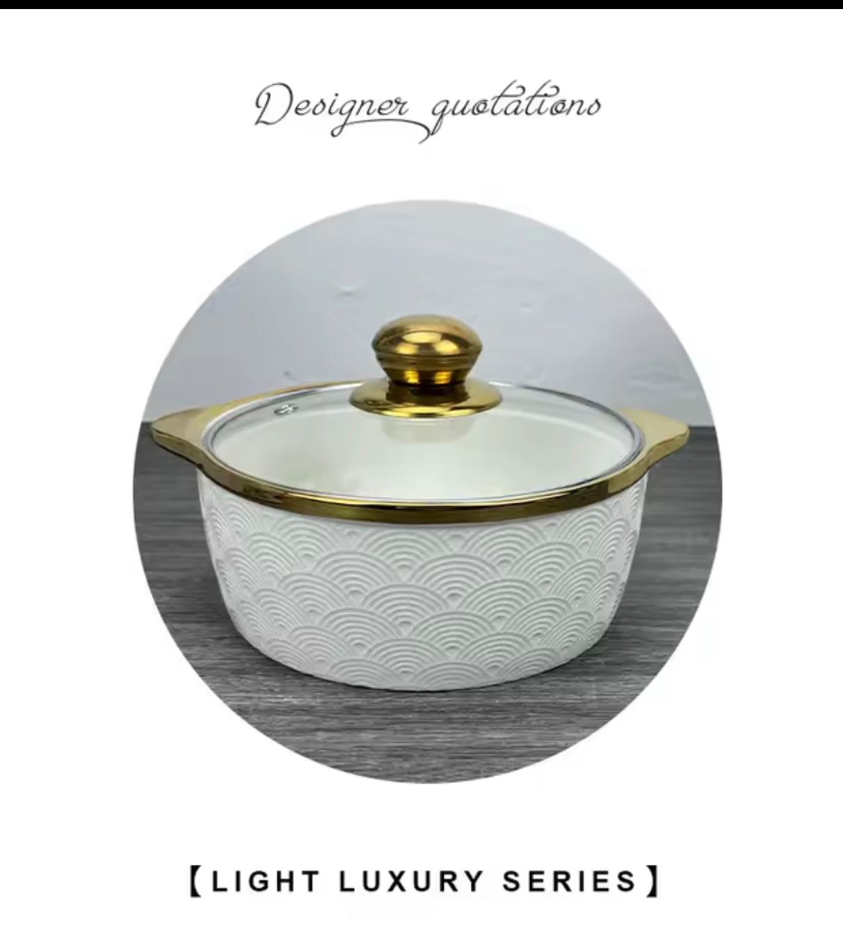 A white ceramic lidded casserole dish with a gold-trimmed glass lid and gold knob, shown inside a circular frame on a gray wood-textured background with decorative text above and below.


