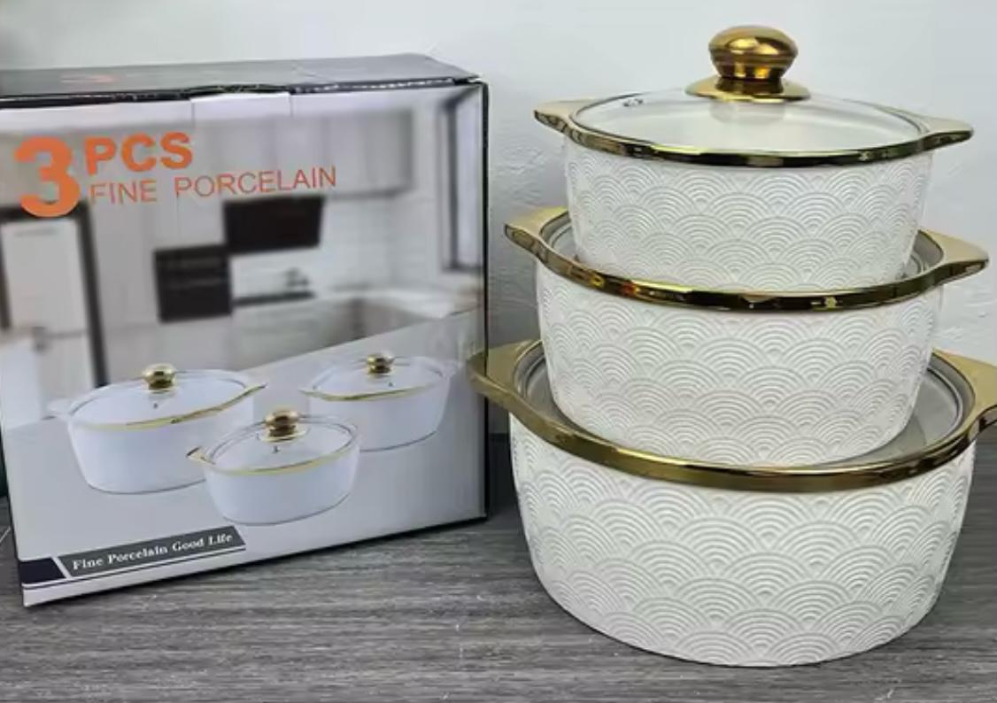 A 3-piece white fine porcelain cookware set with gold trim and lids, shown next to its retail packaging box on a gray wood-textured surface.


