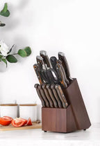 A wooden knife block filled with kitchen knives and scissors, set on a countertop with a blurred kitchen background and tomato slices nearby.

