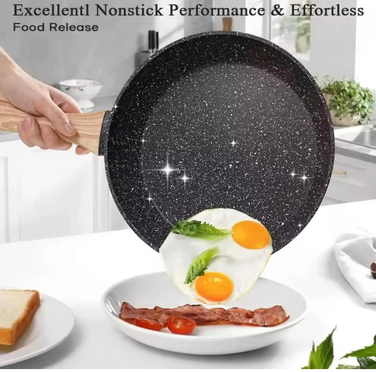 A hand holds a black speckled nonstick frying pan over a white plate containing fried eggs, bacon, and cherry tomatoes, with text at the top reading 'Excellent! Nonstick Performance & Effortless Food Release'.

