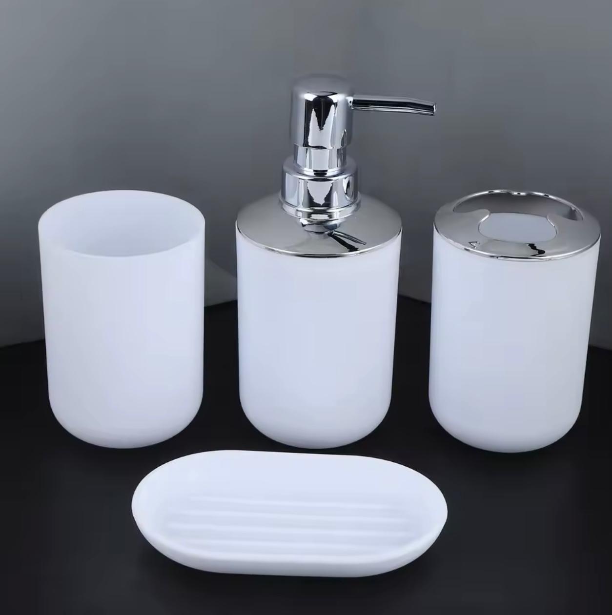 A 4-piece bathroom vanity set in matte white and polished chrome, including a toothbrush holder, a pump dispenser, a tissue box cover, and a soap dish, arranged on a dark surface against a gray background.

