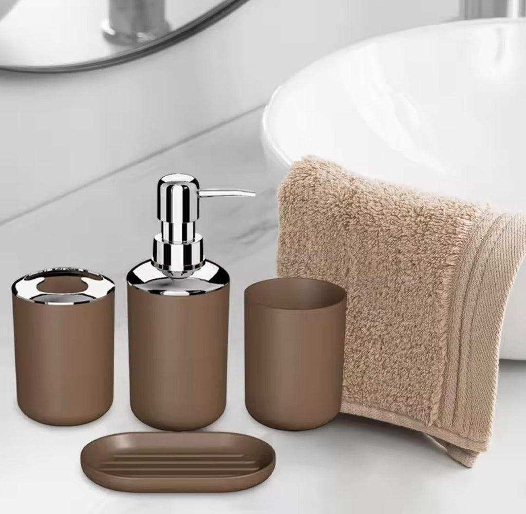 A 4-piece bathroom vanity set in a matte brown finish with polished chrome hardware, including a tooth holder, soap dispenser, cup, and a separate oval soap dish, shown next to a beige towel on a white countertop.

