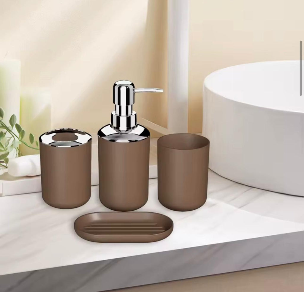 A 4-piece matte brown bathroom vanity set with a chrome pump dispenser, tooth holder, cup, and oval soap dish, arranged on a white marble countertop next to a white sink.

