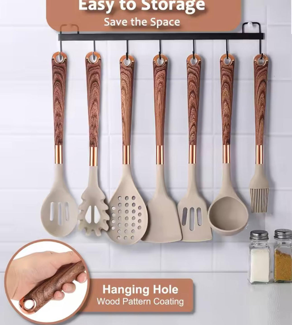 A set of eight kitchen utensils with beige silicone bodies and brown wood-grain patterned handles hang from a black wall rack against a white tiled wall. The image includes marketing text overlays and a circular inset showing a hand holding one of the wooden handles.

