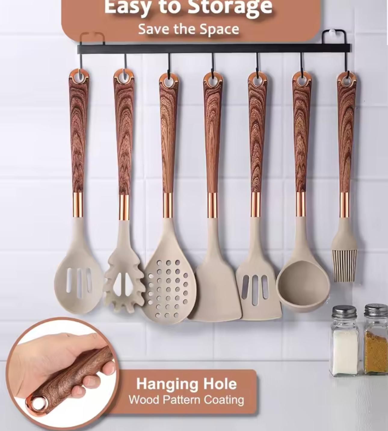 A set of eight kitchen utensils with beige silicone bodies and brown wood-grain patterned handles hang from a black wall rack against a white tiled wall. The image includes marketing text overlays and a circular inset showing a hand holding one of the wooden handles.


