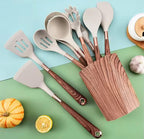 A set of silicone kitchen utensils with dark brown wood-grain handles and a matching wooden utensil holder, arranged on a split light blue and green background with small food props including a pumpkin, lemon, garlic, and a plate.

