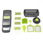 A multi-piece kitchen vegetable chopper and slicer set arranged on a white background. The set includes a dark gray manual mandoline slicer with lime green accents, several interchangeable blade attachments, a black plastic colander basket, a round black lid, a small fork, and two square grid cutting inserts.

