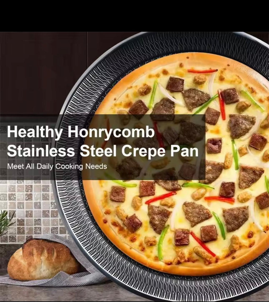A large pizza topped with sausage pieces, green peppers, and red onions sits inside a black stainless steel crepe pan. A bread loaf and a striped cloth are visible in the lower-left corner, with a dark kitchen-style background.

