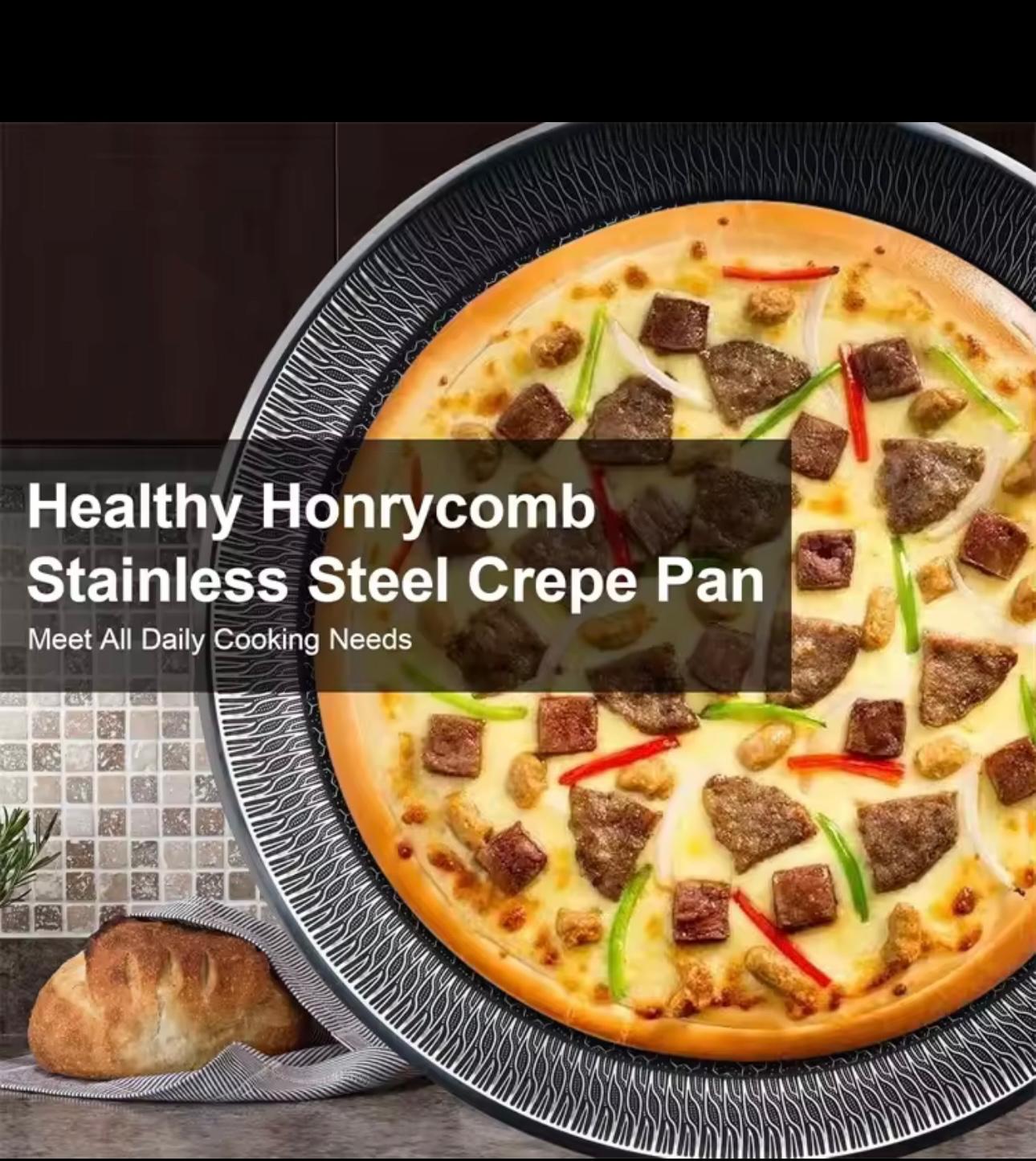 A large pizza topped with sausage pieces, green peppers, and red onions sits inside a black stainless steel crepe pan. A bread loaf and a striped cloth are visible in the lower-left corner, with a dark kitchen-style background.

