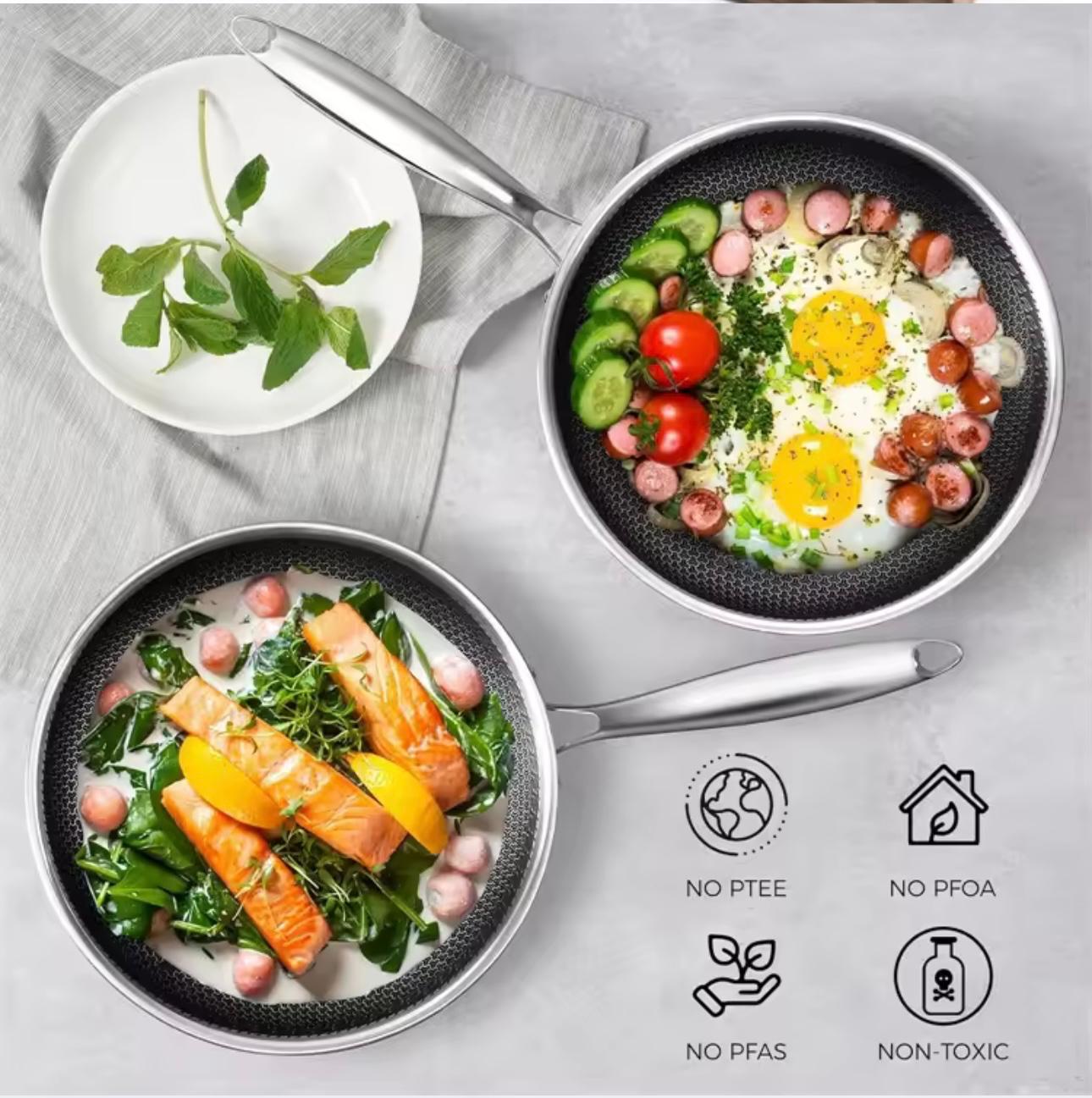 Two frying pans with food on a gray surface, featuring icons for non-PTFE, non-PFOA, no PFAS, and non-toxic.

