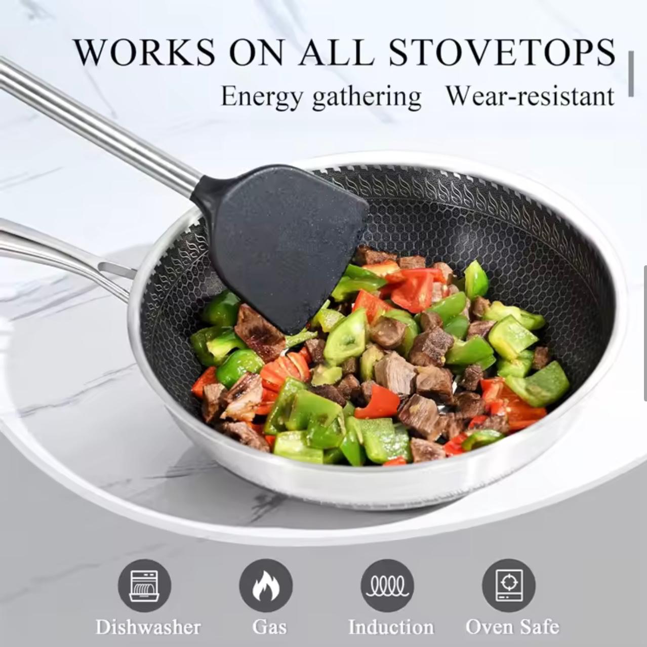A black silicone spatula with a stainless steel handle resting inside a silver non-stick frying pan 