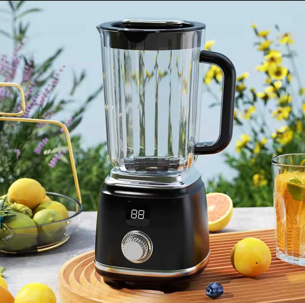 A black countertop blender with a clear pitcher and black handle, shown on a wooden tray outdoors with lemons, a glass of orange drink, and blurred flowers in the background.


