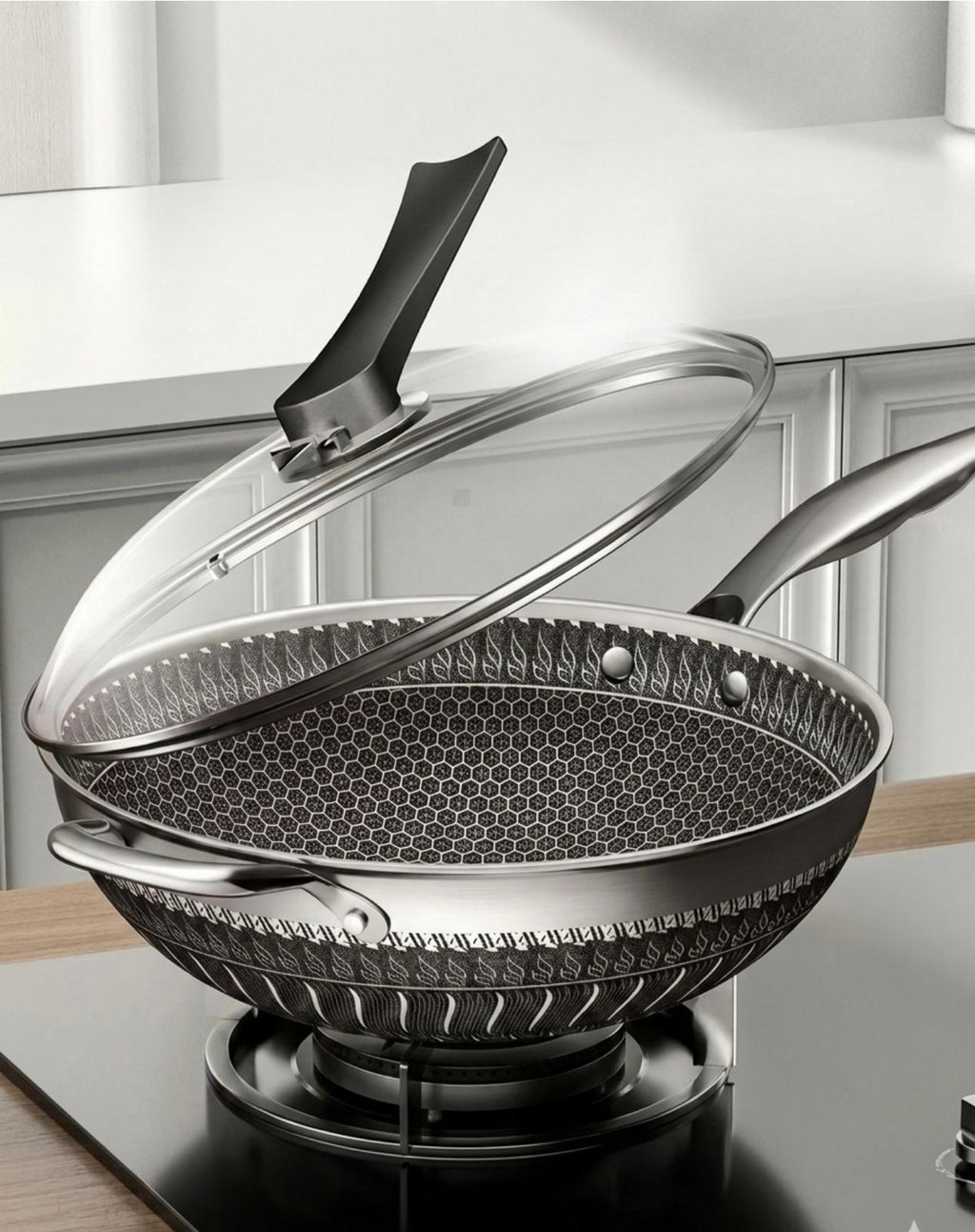 A stainless steel wok with a black handle and a clear glass lid, shown on a stovetop in a kitchen setting.

