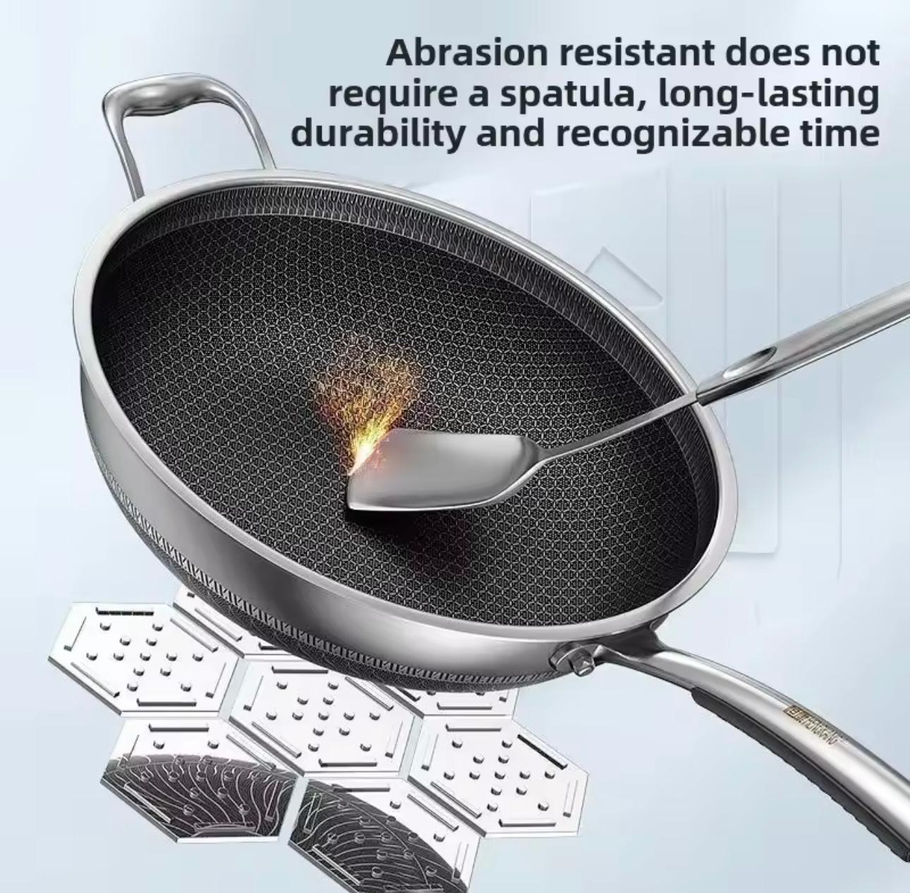 A stainless steel frying pan with a dark textured non-stick interior is shown on a light blue background with marketing text and a spoon resting inside the pan. The text reads, 'Abrasion resistant does not require a spatula, long-lasting durability and recognizable time.

