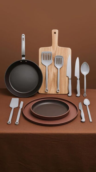 Kitchen utensils and cookware on a brown surface with a wooden cutting board.

